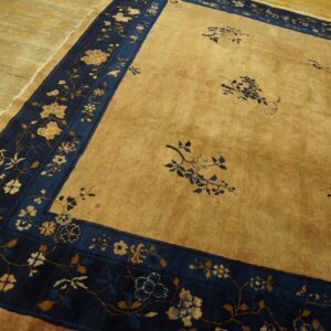 Golden tan rug with a wide navy blue floral border visible on light hardwood planks.