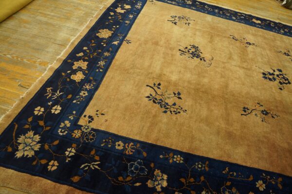 Golden tan rug with a wide navy blue floral border visible on light hardwood planks.