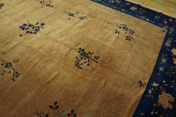 Golden low-pile rug featuring scattered blue floral motifs and a complex navy blue patterned border on a wood floor.