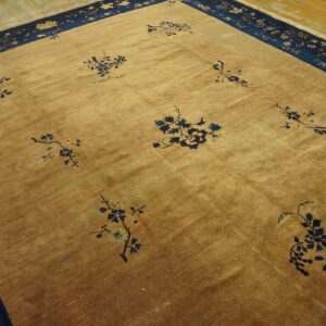 Tan rug with scattered navy floral branches and a wide navy border resting on light wood flooring.
