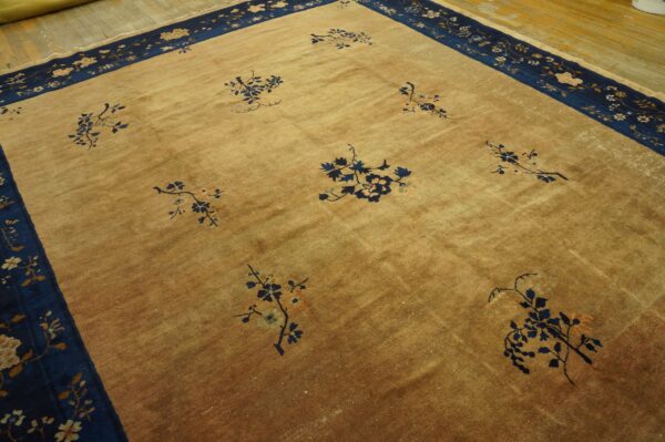 Tan rug with scattered navy floral branches and a wide navy border resting on light wood flooring.