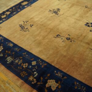 A golden-tan rug featuring blue floral patterns and a wide dark blue border rests on wood floors.