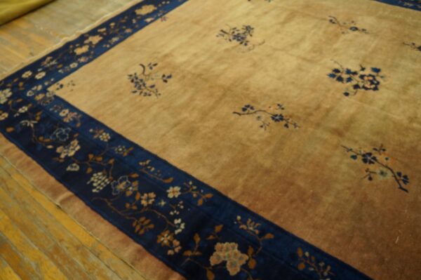 A golden-tan rug featuring blue floral patterns and a wide dark blue border rests on wood floors.