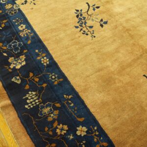 Gold rug with a wide navy blue border stripe featuring floral and vine motifs, sitting on yellow wood floor.