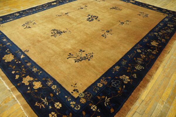 Golden tan rug featuring scattered blue floral designs and a wide navy blue botanical border on wooden flooring.