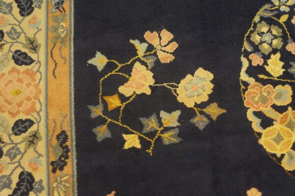 Navy rug field with yellow, peach, and gray floral patterns beside a broad mustard and cream border.