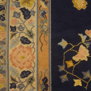 Floral navy rug field meets a wide tan border accented with pink, gold, and slate blue motifs.