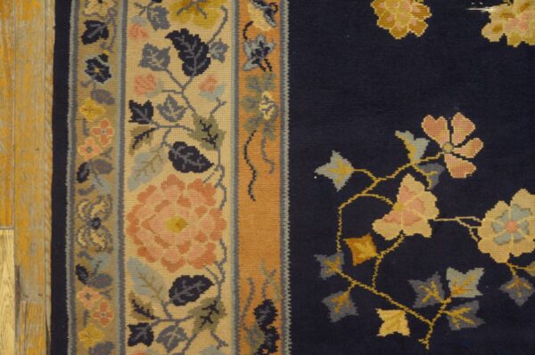 Floral navy rug field meets a wide tan border accented with pink, gold, and slate blue motifs.
