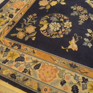 Navy blue floral rug with gold, peach, and rust accents, showing the patterned border on light wood flooring.
