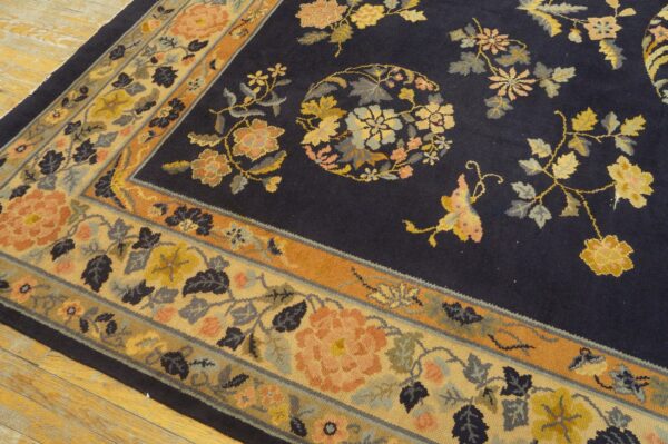 Navy blue floral rug with gold, peach, and rust accents, showing the patterned border on light wood flooring.