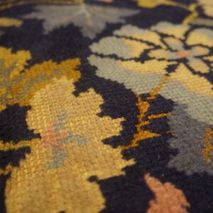 Textured close-up of a navy rug featuring a floral pattern in gold, sage green, and peach tones.