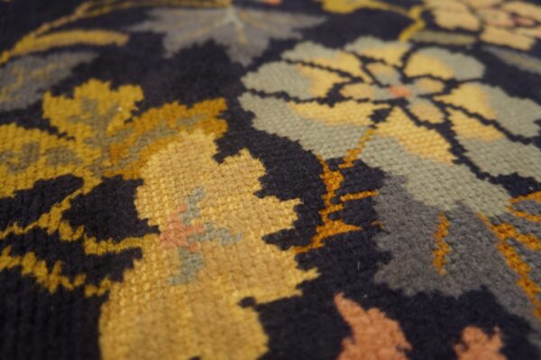 Textured close-up of a navy rug featuring a floral pattern in gold, sage green, and peach tones.