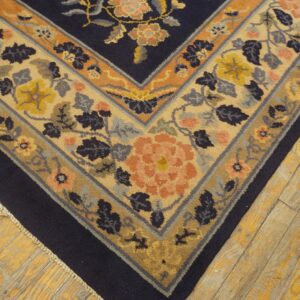 Intricate floral rug corner featuring navy blue, beige, peach, and gold on rustic hardwood floor.