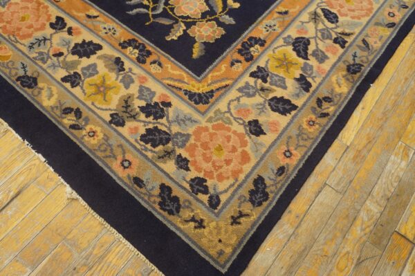 Intricate floral rug corner featuring navy blue, beige, peach, and gold on rustic hardwood floor.