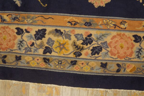 Detailed rug border with salmon, gold, and gray florals against a navy field rests on distressed wood planks.