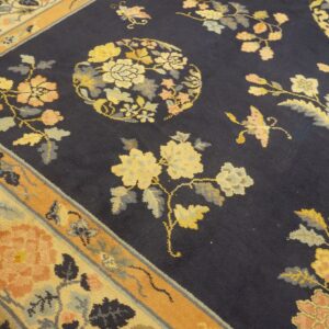 Navy area rug featuring scattered yellow and peach flowers and leaves bordered by orange and cream bands.