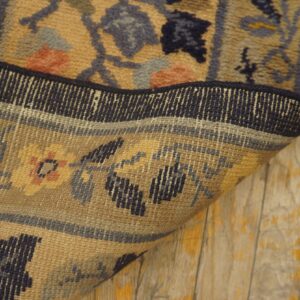 Low-pile tan, blue, and coral patterned rug is folded on painted, distressed wood flooring.