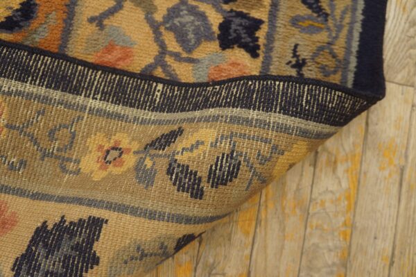Low-pile tan, blue, and coral patterned rug is folded on painted, distressed wood flooring.