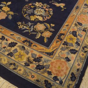 Navy blue floral rug displaying detailed peach and yellow blossoms and a wide patterned border on wood.