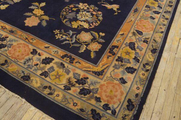 Navy blue floral rug displaying detailed peach and yellow blossoms and a wide patterned border on wood.