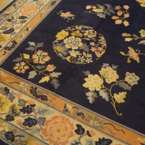 Navy blue rug with floral sprays and a circular medallion rests on distressed wood planks.