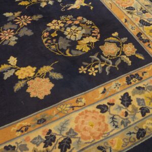 Angled view of a dark navy rug with multicolor floral motifs and wide beige and orange patterned borders.