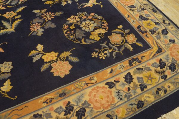 Angled view of a dark navy rug with multicolor floral motifs and wide beige and orange patterned borders.