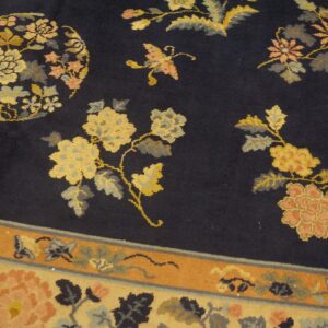 Detailed view of a navy rug featuring large golden yellow and coral floral motifs and a patterned border.