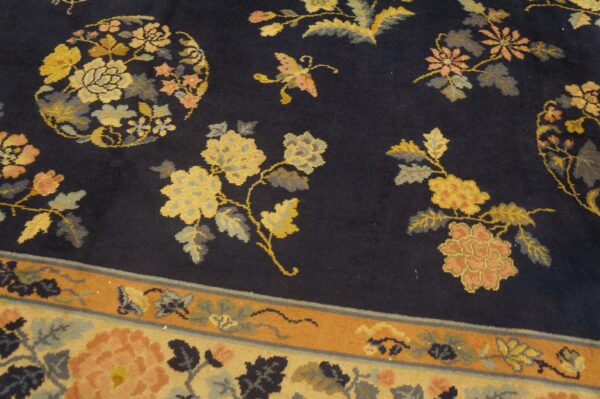Detailed view of a navy rug featuring large golden yellow and coral floral motifs and a patterned border.