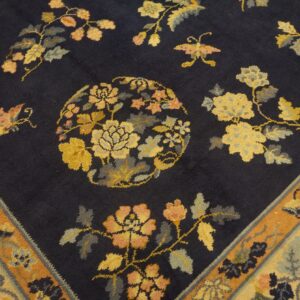 Detail view of a navy rug with yellow, peach, and grey botanical designs and a wide orange border.
