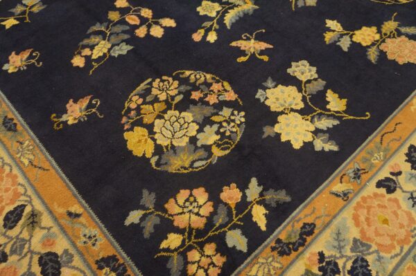 Detail view of a navy rug with yellow, peach, and grey botanical designs and a wide orange border.
