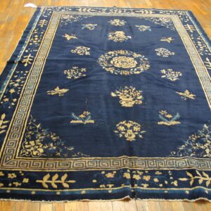 Deep blue rug with gold floral patterns and geometric borders displayed on hardwood planks.