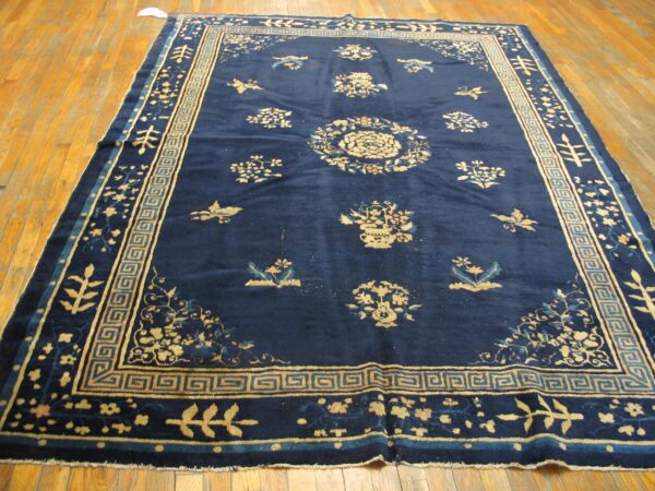 Deep blue rug with gold floral patterns and geometric borders displayed on hardwood planks.