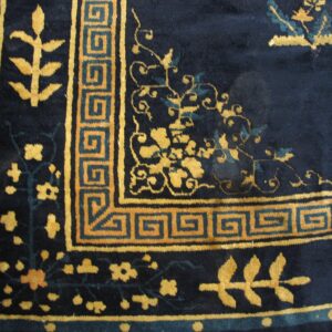 Plush navy rug detail showing gold botanical patterns and a geometric meander border design.