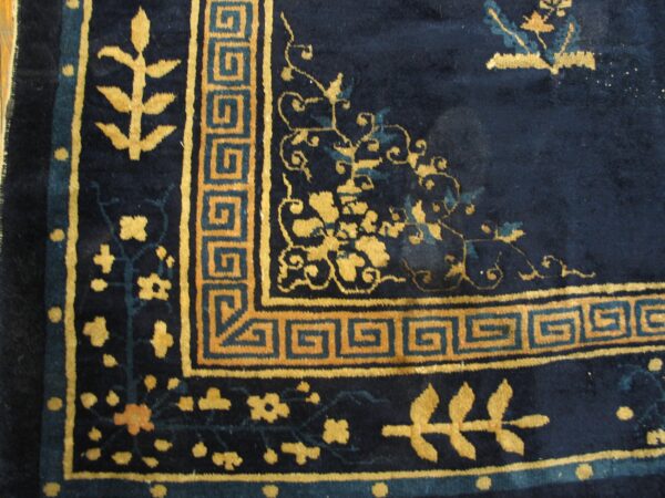 Plush navy rug detail showing gold botanical patterns and a geometric meander border design.