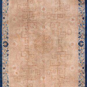 Tan rug featuring faded geometric motifs, a central symbol, and a wide border of deep blue florals.