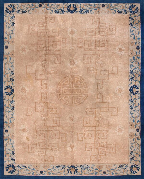 Tan rug featuring faded geometric motifs, a central symbol, and a wide border of deep blue florals.