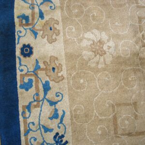 Beige rug with a dark blue border and blue floral motifs resting on distressed wood flooring.