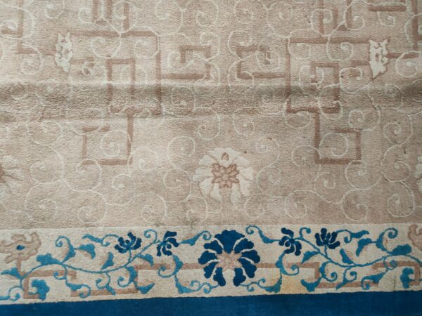 Detail of a rug showing a light tan field pattern and a deep blue and teal floral border.