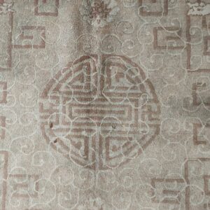 Low-pile beige rug detailed with faded reddish-brown geometric key patterns and a prominent central medallion.