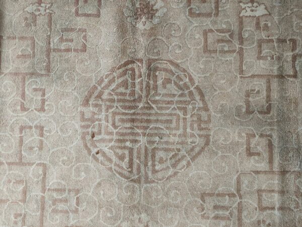 Low-pile beige rug detailed with faded reddish-brown geometric key patterns and a prominent central medallion.