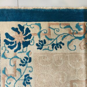 High-pile rug corner with a teal border, cream field, and pink and blue floral geometric pattern on white tile.