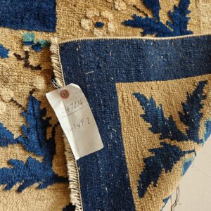 High-pile tan and indigo rug with floral pattern folded over its flat-woven reverse, including an inventory tag.