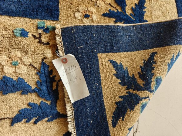 High-pile tan and indigo rug with floral pattern folded over its flat-woven reverse, including an inventory tag.