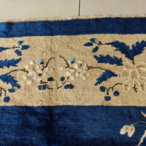 Blue, beige, and cream rug border with dense floral and foliage motifs and visible fringe.
