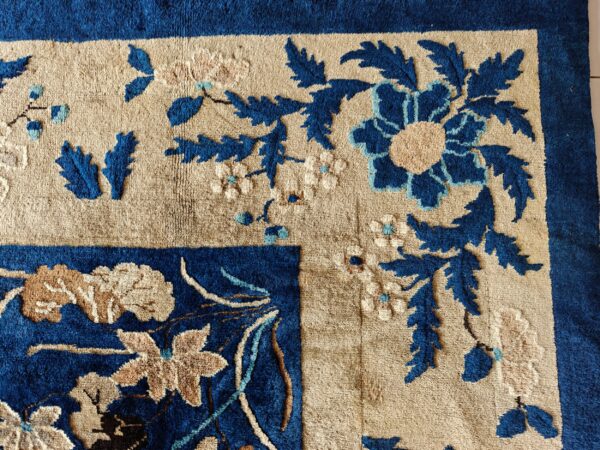 Close-up of a high-pile rug featuring a beige field and bold blue, floral, and botanical motifs.