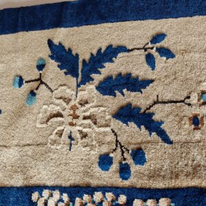 Textured high-pile rug detail features sculpted floral patterns in blue, teal, and brown on a beige field.