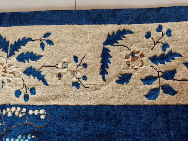 Detail of a high-pile rug with a royal blue border framing a tan field with blue and brown floral vines.