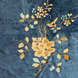 Close-up of a textured dark blue rug featuring a tan and mint floral vine motif.