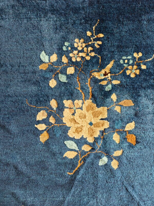 Close-up of a textured dark blue rug featuring a tan and mint floral vine motif.